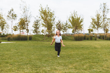 a little cheerful girl with long hair runs through the grass in the park and rejoices.