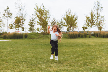 Fototapeta premium a little cheerful girl with long hair runs through the grass in the park and rejoices.