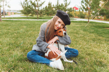 a little girl kisses and hugs her Jack Russell terrier dog in the park. Love between the owner and the dog. a child is holding a dog in his arms.