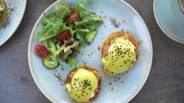 Top view of a plate with gourmet eggs benedict and vegetable salad
