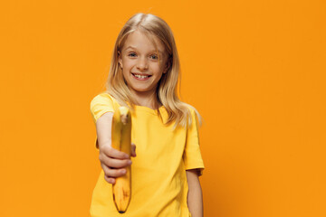 cute, shy, beautiful school-age girl in yellow clothes stands against a bright, yellow background,...