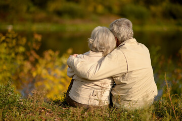 Elderly couple sitting on the grass in autumn. Back view.