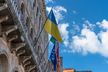 The flag of Ukraine, the flag of the European Union, the flag of Italy and Venice are fluttering in the wind on the wall of an old historical building against the blue sky in the city of Venice