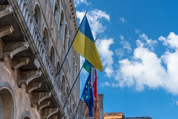 Fototapeten The flag of Ukraine, the flag of the European Union, the flag of Italy and Venice are fluttering in the wind on the wall of an old historical building against the blue sky in the city of Venice © Александр Бочкала