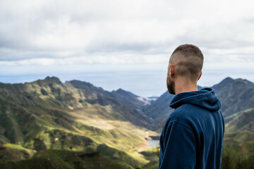 Naklejka na ściany i meble Backwards of caucasian young man with blue hoodie and cloudy day, looking the landscape