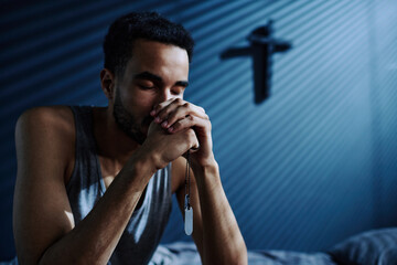 Young depressed man with metallic medallions on chain in his hands praying God to help him get...