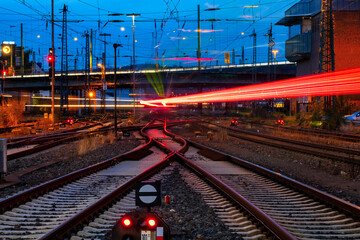 Blue hour at the Station of Hagen Westphalia Germany with many lights, signals and trains in motion. Railway infrastructure and technology. Crossings, catenary, glistening tracks, switches at twilight