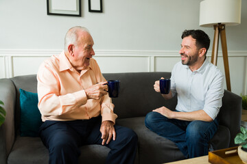 Excited elderly father and son chatting drinking coffee at home