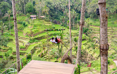 An Asian couple sitting on swing over Tegalalang Rice Terrace is one of the famous tourist objects...