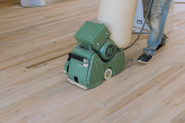 Using floor sander contractor grinds a wooden parquet floor in newly constructed home, using the...
