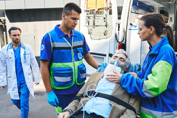 Doctor rushing to senior patient with breathing mask on ambulance stretcher who was brought by...