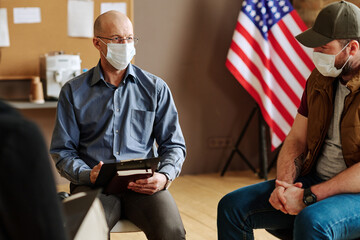 Mature male psychotherapist in protective mask listening to patients with post traumatic syndrome...