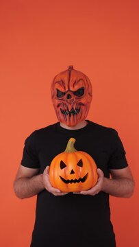 Person with pumpkin mask celebrating Halloween, holding a pumpkin, on orange background. Concept of celebration, All Souls' Day and All Saints' Day.	