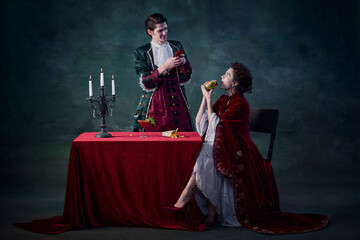 Fototapeta premium Portrait of man and woman in image of vampires over dark green background. Man taking selfie of woman eating burger