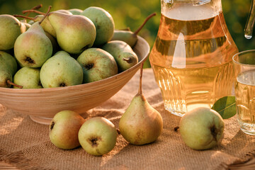 A glass with pear juice and basket with pears on wooden table with natural orchard background on sunset light. Vegetarian fruit composition