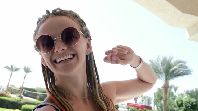 Happy smiling girl joyfully making excited selfie video call in summer vacation, young crazy woman with dreadlocks taking selfies in round sun glasses, slow motion