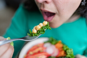 Woman mouth about to eat some of her vegetarian lunch. Close up caption. Selective focus