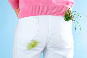 The girl standing with a dirty grass stain on her white pants with her back turned on a blue...