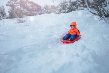 Fototapeta na wymiar Cute boy in orange ski sport outfit go downhill on the sledge