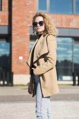 Portrait of a young Caucasian girl in a coat and sunglasses in the city on an autumn day.