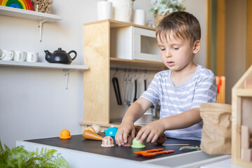 Cute male kid preparing toy food boiling vegetables on cooker at childish room kitchen