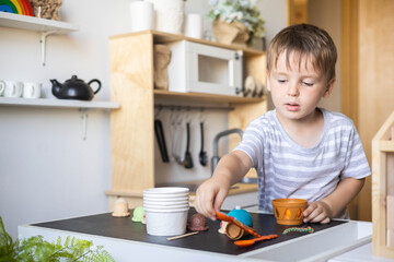 Cute male kid preparing toy food boiling vegetables on cooker at childish room kitchen