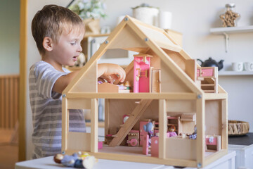 Cute male kid playing toy doll house with interior furniture Montessori wooden eco friendly material