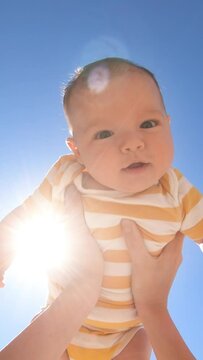 Mother throwing baby up against the blue sky. Happy woman enjoying motherhood with her little son outdoors. POV, vertical video