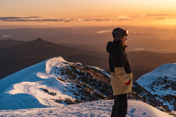 hiker starring at the sunset on top of snowy mountain