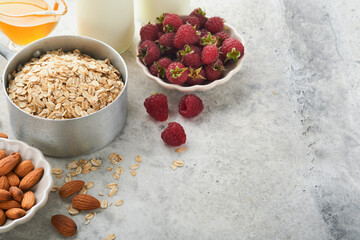 Ingredients for cooking oatmeal or granola with oats, milk, raspberries, honey and almonds on gray concrete old table background. Ingredients for healthy breakfast.