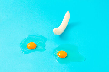 Peeled banana and two broken eggs on a blue background. Minimal creative concept.