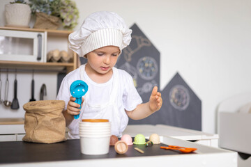 Cute male kid preparing toy food boiling vegetables on cooker at childish room kitchen
