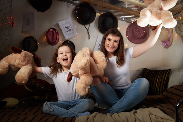 Brunette mother and little child having fun with toy dogs on the bed together. Happy family