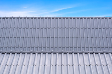 Two gray corrugated fiber cement tile roofs in different level against blue sky background