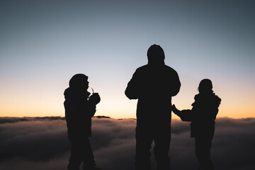 three person silhouette watching the sunrise over the clouds