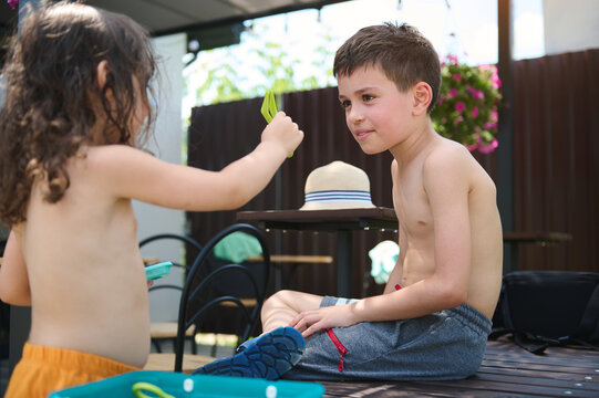 Charming adorable Caucasian children, a boy and girl, brother and sister, friends talking together, playing on a summer terrace on a hot sunny summer day