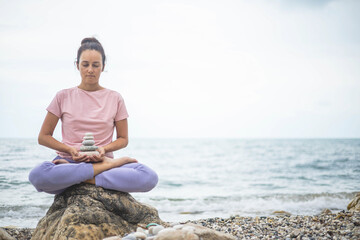 Naklejka na ściany i meble Spiritual yoga woman lotus position on cobblestone with pebble tower harmony relax meditation beach