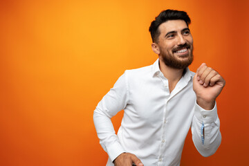 Young man celebrating and dancing against orange background in studio