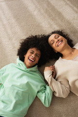 top view of happy african american girl smiling while lying on carpet with positive mother.