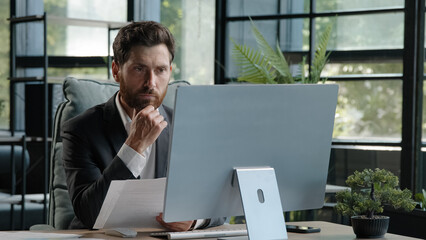 Caucasian pensive bearded man boss manager adult 40s businessman sitting in office busy with...