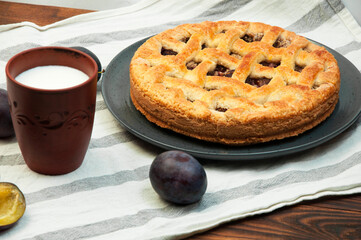shortbread cookies with plums and a glass of milk on a wooden table. concept of homemade shortcrust pastry. baked fruit dessert on the kitchen table with a drink close up