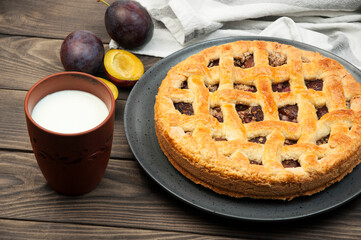 shortbread cookies with plums and a glass of milk on a wooden table. concept of homemade shortcrust pastry. baked fruit dessert on the kitchen table with a drink close up