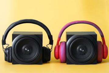 Two black one-way audio speakers and two wireless headphones with ear pads on a yellow background. Concept of a musical duet, audio podcasts and broadcast for two. Copy space.