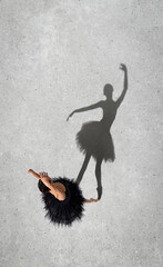 Portrait of young ballerina in black dress performing isolated over grey wall background. Top view. Shadow element