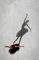 Portrait of young ballerina in black dress performing isolated over grey wall background. Top view. Shadow element. Elegance and grace