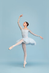 Portrait of tender young ballerina dancing, performing isolated over blue studio background. Graceful theatrical performance