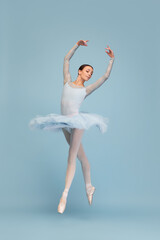 Portrait of tender young ballerina dancing, performing isolated over blue studio background. Beauty of choreography
