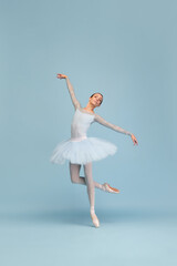 Portrait of tender young ballerina dancing, performing, posing in movement isolated over blue...
