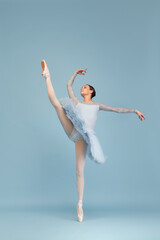 Portrait of tender young ballerina dancing, performing isolated over blue studio background. Standing on twine