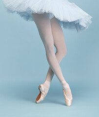 Cropped image of female legs, ballerina in tutu and pointe standing on tiptoe isolated isolated over blue studio background